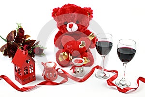 Valentine`s Day concept. Red teddy bear with red wine and heart shaped candle with red ribbon and red roses on isolated white back