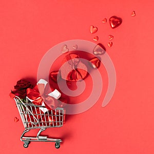 Valentine's day concept. Shopping trolley with gift boxes, roses, chocolate and red hearts on red background