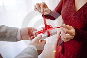 Valentine`s day concept. Side view of a woman opening a giftbox with red ribbon in hands. Loving couple give each other presents