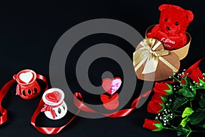 Valentine`s day concept. Teddy bear in heart shaped gift box with candle and red roses on black background.