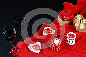 Valentine`s day concept. Teddy bear in heart shaped gift box with candle and red wine on black background.