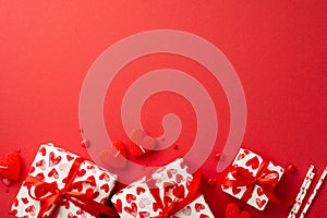 Valentine`s Day concept. Top view photo of gift boxes heart shaped candles straws and sprinkles on isolated red background with