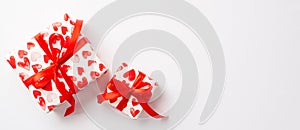 Valentine`s Day concept. Top view photo of gift boxes in wrapping paper with heart pattern and red ribbon bows on isolated white