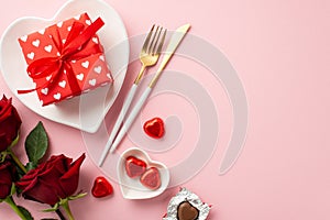 Valentine`s Day concept. Top view photo of heart shaped tableware present box knife fork chocolate candies and bouquet of roses o