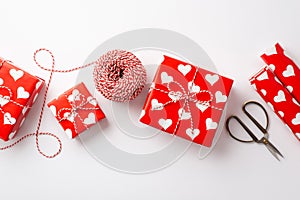 Valentine`s Day concept. Top view photo of present boxes wrapping paper rolls spool of twine and scissors on isolated white