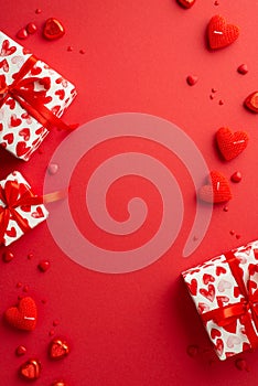 Valentine`s Day concept. Top view vertical photo of gift boxes heart shaped candies candles and sprinkles on isolated red