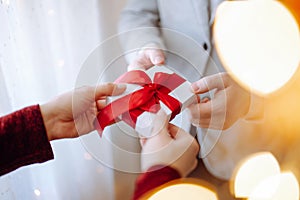 Valentine`s day concept. Young romantic couple holding a gift in their hands with a garland lights bokeh on the front. White