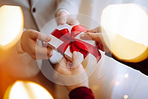 Valentine`s day concept. Young romantic couple holding a gift in their hands with a garland lights bokeh on the front. White