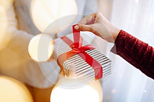 Valentine`s day concept. Young romantic couple opening a gift in their hands with a garland lights bokeh on the front. White