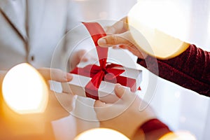 Valentine`s day concept. Young romantic couple opening a gift in their hands with a garland lights bokeh on the front. White