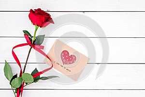 Valentine`s day congratulation. Red rose and greeting card with heart sign on white wooden background top view copy