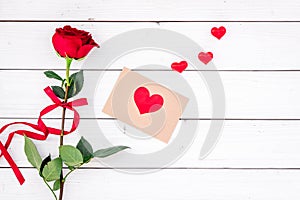 Valentine`s day congratulation. Red rose and greeting card with heart sign on white wooden background top view copy