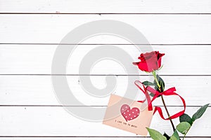 Valentine`s day congratulation. Red rose and greeting card with heart sign on white wooden background top view copy