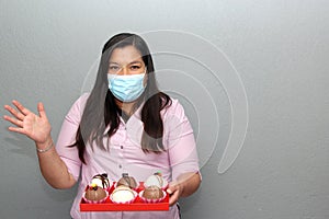 Valentine`s day in contingency covid-19. latin woman with protection mask and chocolate bombs in red ragalo base