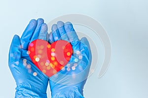 Valentine`s Day during the coronavirus pandemic. Hands in medical blue gloves hold a red heart on a blue background