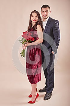 Valentine`s Day couple with roses on beige background. Portrait of happy young lovers with flowers. Picture showing man giving