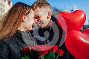 Valentine`s day date. Man and woman about to kiss in city. Couple walking with roses flowers and balloons