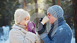 Valentine's day date. Young stylish loving couple drink coffee or hot tea walking in winter park.