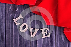 Valentine`s day elegant still life with love lettering and red fabric on wooden background photo