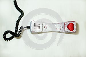 Valentine's Day February 14 telephone receiver on a wire vintage old lies on a white scratched texture background red heart heard