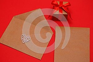 Valentine`s Day, February 14th a figured, wooden, white heart on an envelope on a red background, next to a gift in a package tie