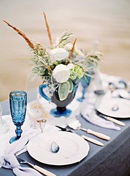 Valentine`s day. Fine art dinner on a beach. Blue wedding. Catering. Wedding bouquet with tender flowers in vase on table