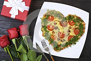Valentine`s day food. Heart shaped pizza next to a gift and red roses, on a dark wooden background. Valentine`s day concept Top
