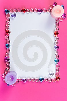 Valentine`s day frame on a pink background made of pebbles in the shape of a heart with white space and candles in the corners