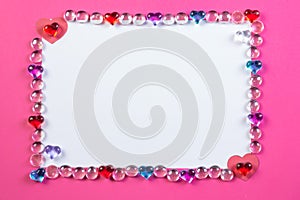 Valentine`s day frame on pink background made of pebbles in the shape of a heart with white space and paper hearts.