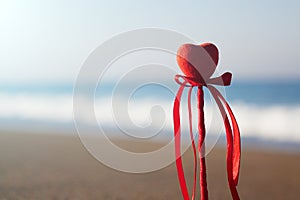 Valentine`s day greeting card concept, red heart on pristine sandy beach, honeymoon vacation background.