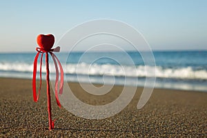 Valentine`s day greeting card concept, red heart on pristine sandy beach, honeymoon vacation background. symbol of love