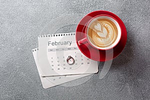 Valentine`s Day greeting card. Red coffee cup, ring and gift box over february calendar. View from above