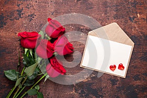 Valentine`s day greeting card Red rose flowers bouquet and craft envelope with red hearts on a vintage wooden background