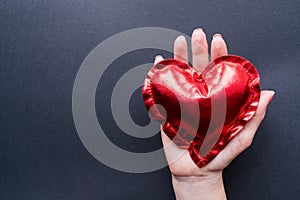 Valentine`s Day. The Hand of a girl holds a red heart on a dark background. Flat Lay top view closeup.