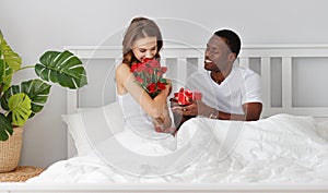 Valentine`s Day. happy couple with red hert and flowers in bed