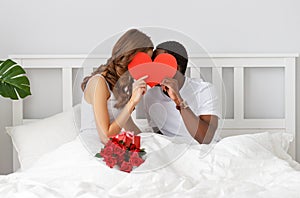 Valentine`s Day. happy couple with red hert and flowers in bed