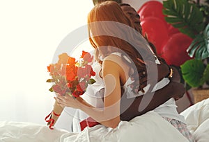 Valentine`s Day. happy couple with red hert and flowers in bed