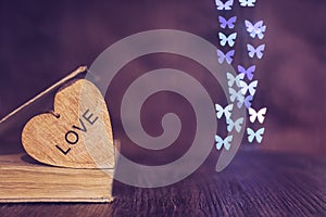 Valentine`s day. Heart book bokeh of butterflies. Wooden heart with the word love.