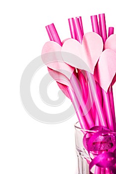 Valentine`s day holiday. bright pink drinking straws with hearts and a pink ribbon in a glass isolated on white.bright sipping st