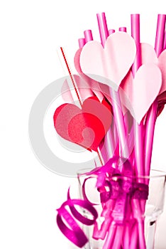 Valentine`s day holiday. bright pink drinking straws with hearts and a pink ribbon in a glass isolated on white