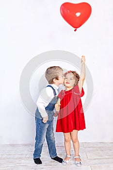 Valentine`s day kids. Boy kisses girl five years old holding red ball heart