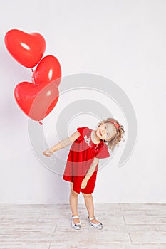 Valentine`s day kids. Little girl in red dress holding heart shaped balloons