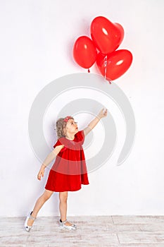 Valentine`s day kids. Little girl in red dress holding heart shaped balloons