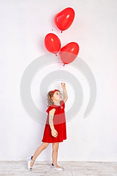 Valentine`s day kids. Little girl in red dress holding heart shaped balloons