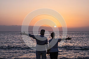 Valentine`s day love couple concept with senior aged people open arms with ocean and sunset in front of them - together forever i