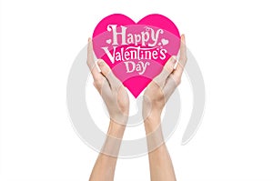 Valentine's Day and love theme: hand holds a greeting card in the form of a pink heart with the words Happy Valentine's day