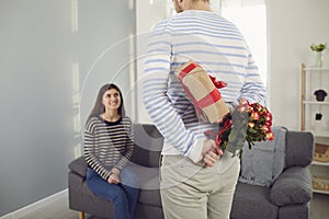 Valentine`s day. Rear view of a man holding flowers and gives a girl a gift in his hands