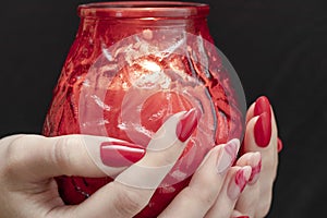 Valentine`s day, red candle in the hands. Red manicure. Black background. Candle fire in the dark