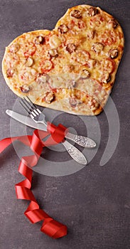 Valentine`s day romantic dinner. Pepperoni pizza, cutlery and scarlet ribbon on dark table