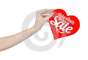 Valentine's Day and sale topic: Hand holding a card in the form of a red heart with the word Sale isolated on white background
